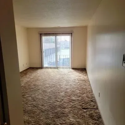 An empty living room with a sliding glass door and blinds.