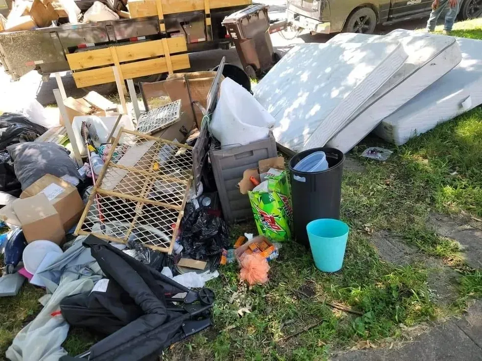 A pile of trash is sitting on the grass next to a sidewalk.