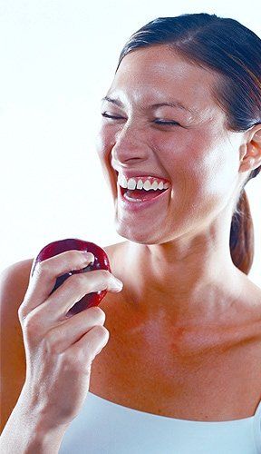 Dental Implants Cost — Woman Holding Apple in Roseville, MI