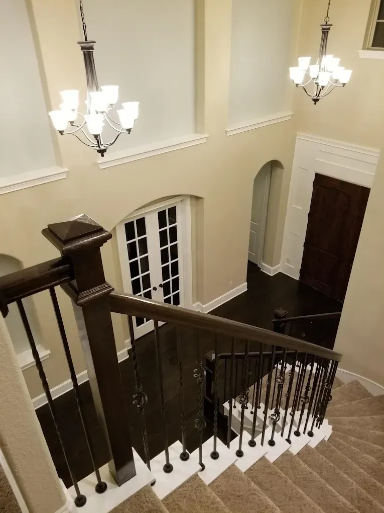 Staircase interior with dark wood and white trim, two chandeliers, and a view of entry doors.