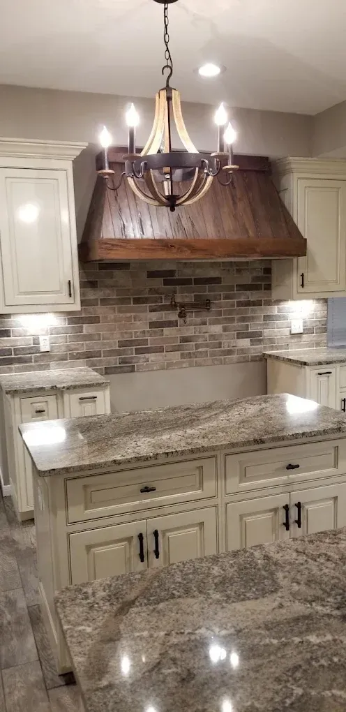 Kitchen with cream cabinets, brick backsplash, wooden range hood, and granite countertops.
