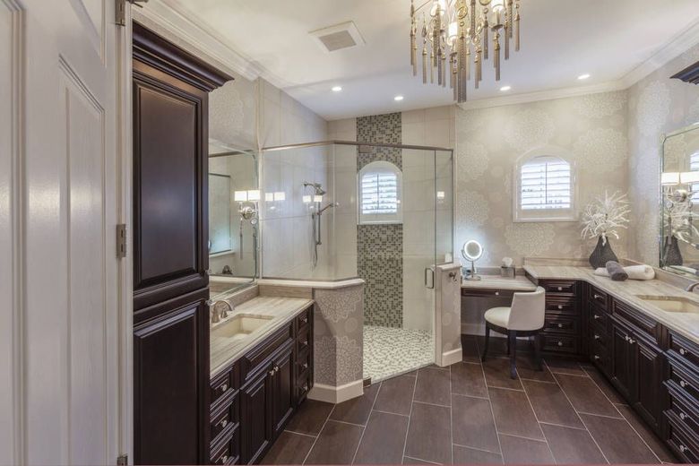 Luxurious bathroom with dark cabinets, glass shower, vanity area, and chandelier.