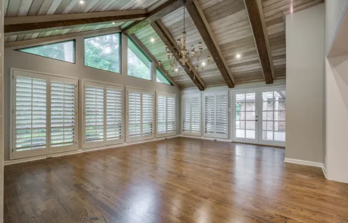 Spacious room with wood floor, high sloped ceiling, large windows, and white shutters.