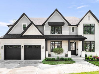 Modern two-story house with white brick, black trim, and gray roof. Two-car garage, manicured landscaping.
