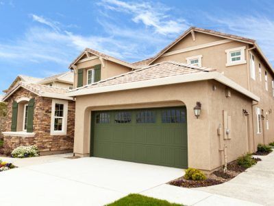 Tan stucco house with green garage door, stone accents, and blue sky.