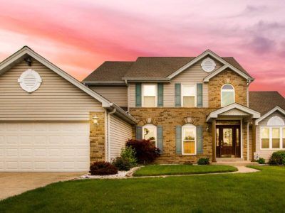 Two-story house with brick and siding, green lawn, driveway, and colorful sunset sky.
