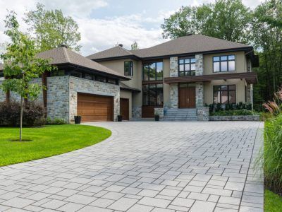 Elegant two-story house with stone and beige facade, curved driveway, and lush landscaping.