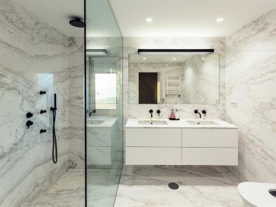 Modern marble bathroom with glass shower, floating vanity, black fixtures.