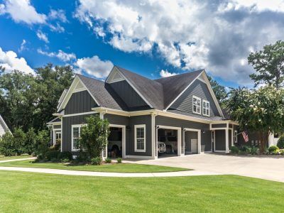 Three-car garage with dark gray siding, white trim, and a gabled roof. Green lawn under a cloudy blue sky.