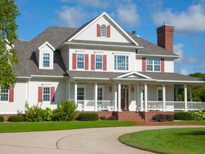 White two-story house with red shutters and brick chimney, surrounded by green grass and a winding driveway.