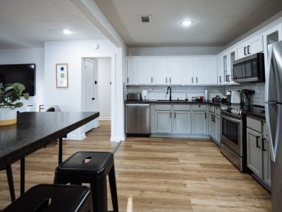 Modern kitchen with white cabinets, stainless steel appliances, and wood flooring.