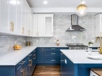 Blue and white modern kitchen with marble backsplash, stainless steel range, and gold hardware.
