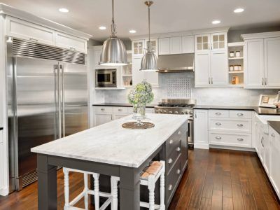 White kitchen with dark island and stainless steel appliances; hanging silver lights.