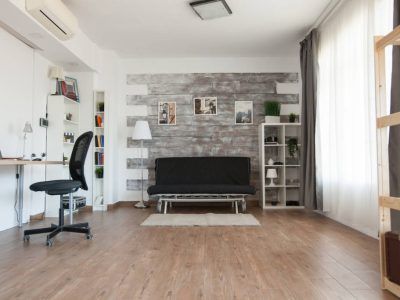 Living room with wood floors, black futon, and a desk with a black chair. White shelves and accent wall.