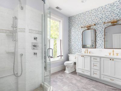 Bright white bathroom with marble shower, vanity with two sinks, and patterned wallpaper.