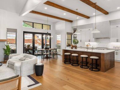 Open-concept kitchen and living area with hardwood floors, white walls, and wooden beams.