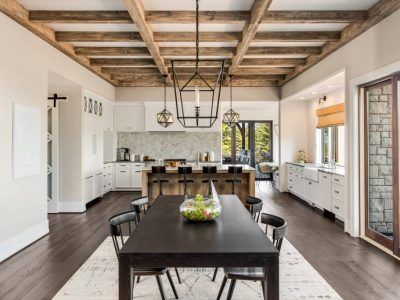 A modern kitchen and dining room with wood beams, white cabinets, and a dark wooden dining table.