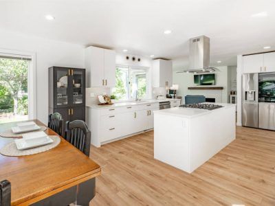 Modern white kitchen with a stainless steel appliance, wooden floors, and a dining table.