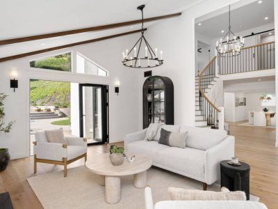 Bright living room with white walls, wood floors, and vaulted ceiling, with open doors to the backyard.
