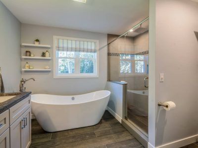 Modern bathroom with white tub, walk-in shower, gray walls, and window.