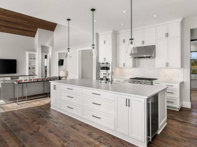 Bright white modern kitchen with large island, stainless steel appliances, and wood flooring.