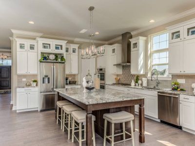 Bright white kitchen with large island, granite countertop, stainless steel appliances, and wood flooring.