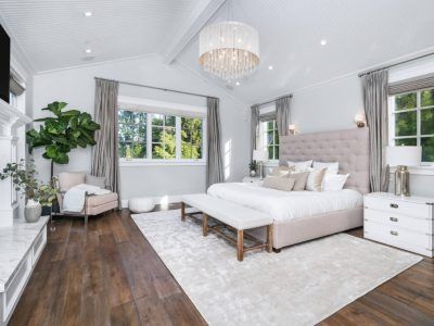 Elegant bedroom with a large bed, chandelier, and a large window overlooking trees.