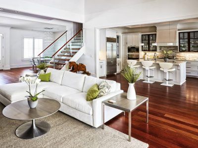 Spacious, modern living room with white sectional, open kitchen, hardwood floors, and glass staircase.