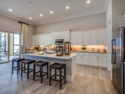 Modern white kitchen with island, stools, and stainless steel appliances.