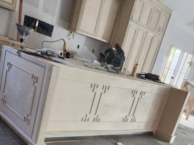 Kitchen island with light-colored cabinets under construction; worker in the background.