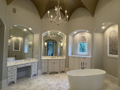 Elegant bathroom with freestanding tub, marble floors, arched mirrors, chandelier, and a gold-painted ceiling.