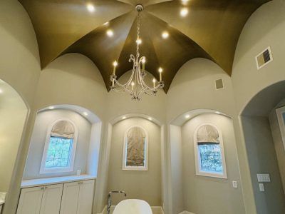 Gold-toned arched ceiling with chandelier; windows with shades; neutral walls; white cabinets.