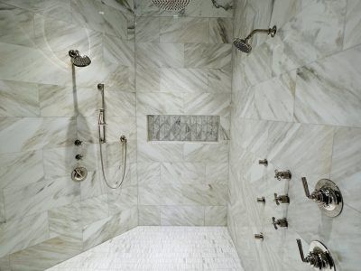 Luxurious marble-tiled shower with multiple showerheads and fixtures, in a bright, modern bathroom.