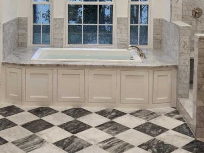 Bathroom with white tub, marble backsplash and walls, and checkered black and white floor.