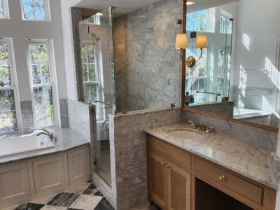 Luxurious bathroom with marble surfaces, shower, vanity, and large windows.