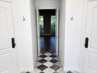 Hallway with black and white checkered floor, white doors, and a room with windows at the end.