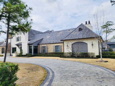 Large, elegant house with stone and cream facade, a winding driveway, and a slate roof.