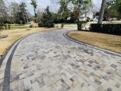 Brick driveway curving toward a house, bordered by dark gray bricks and brown grass.