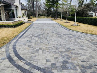 Paver driveway with curved dark border. Beige and gray brick pattern leads to a home.