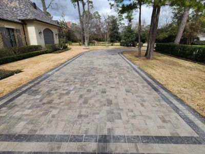 Brick driveway leading to a house, with green landscaping on both sides.