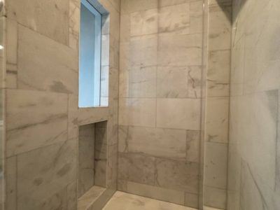Marble-tiled shower with a niche and window. White and gray tones, modern design.
