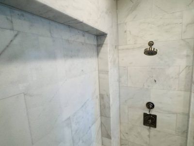Marble-tiled shower interior with a built-in shelf and showerhead with controls.