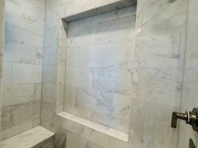 Marble-tiled shower with built-in shelf. White with gray veining. Bench seat on left.