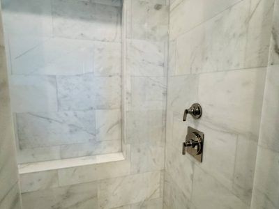 Marble-tiled shower interior with a built-in shelf and chrome fixtures.