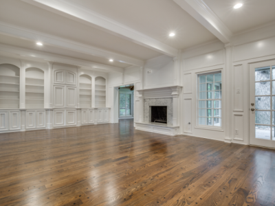 Empty, bright living room with built-in shelves, fireplace, and hardwood floors. White walls and trim.