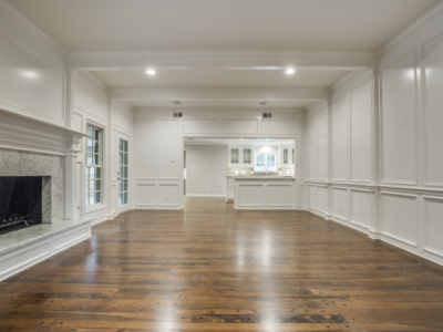 Empty, white-walled room with dark hardwood floors, fireplace, and arched entry to a kitchen.