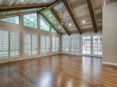 Empty room with hardwood floors, wooden ceiling beams, and shuttered windows.