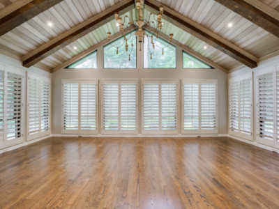 Empty room with wooden floors, white shutters, and a vaulted, wood-paneled ceiling.