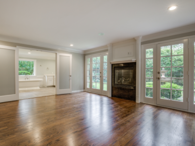 Empty room with dark wood floors, fireplace, and glass doors leading to the outdoors and a bathroom.