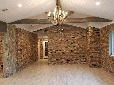 Brick-walled interior with light wood floors, a white ceiling with beams, and a chandelier.